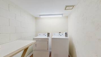 A laundry room with two stacked washers and dryers, a wooden bench, and a fluorescent light fixture.