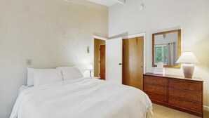 Een slaapkamer met een bed, een dressoir, een spiegel en een deur die naar een andere kamer leidt.