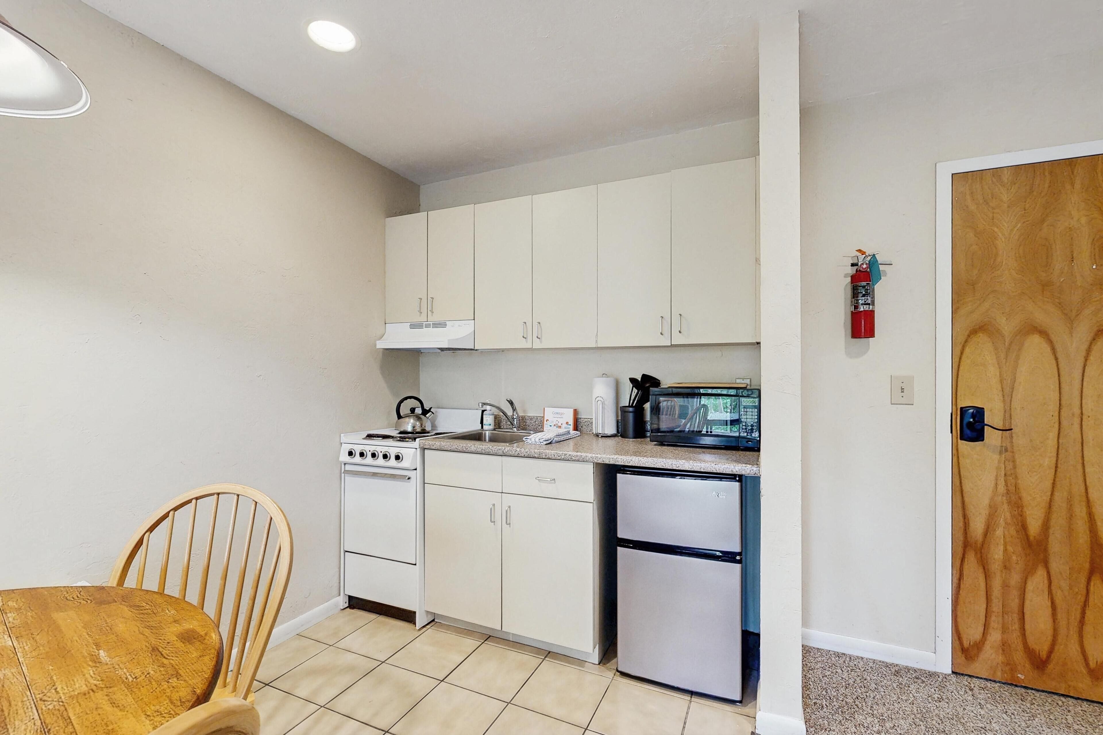 A compact kitchen with white cabinets, a stove, a microwave, and a refrigerator.
