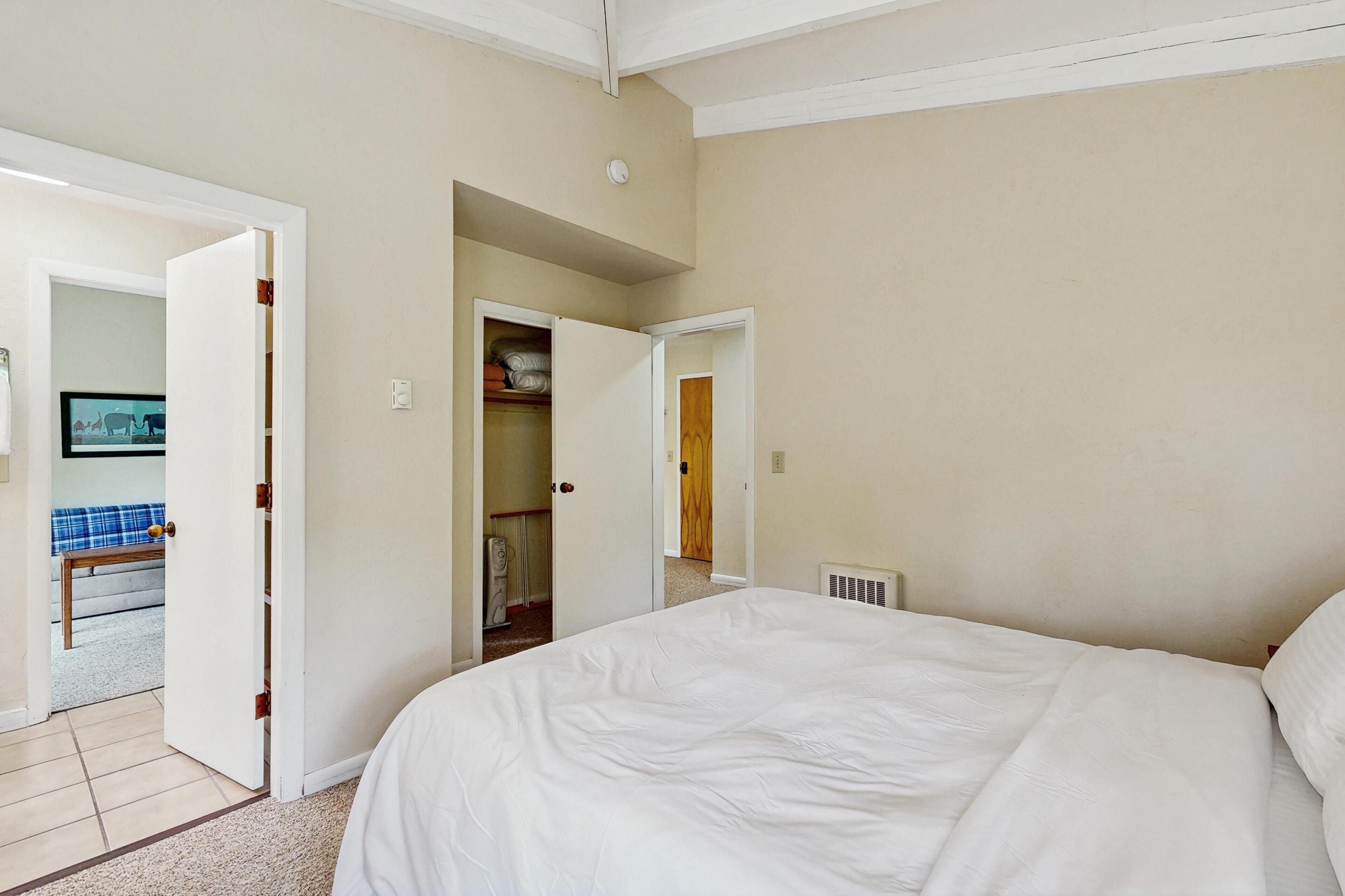 A bedroom with a large bed, a closet with open doors, and a visible television in another room.