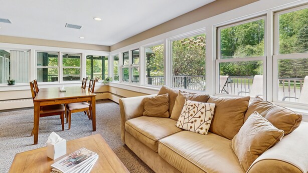 A spacious room with a large window, a beige sofa, a wooden dining table, and a small coffee table. - Four Season Connecting Condos:  seasonal pool, ski, hike & golf (Warren)