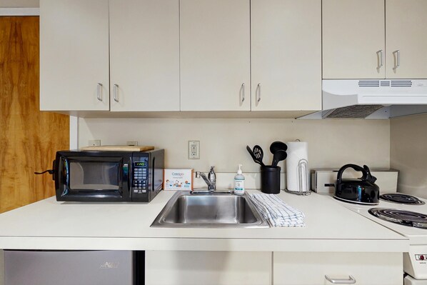 A kitchen with a microwave, sink, kettle, and various utensils.