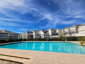 Ein Pool mit Fliesen umgeben, von mehrstöckigen Gebäuden mit Balkonen gesäumt, unter blauem Himmel.