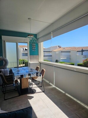 Un balcon avec une table et des chaises, un luminaire suspendu et une vue sur les bâtiments voisins.