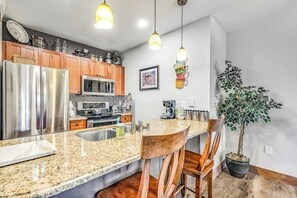 Eine Küche mit Granit-Arbeitsplatten, Edelstahlgeräten, Holzschränken und Pendelleuchten.