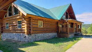 A log cabin with a stone foundation, a porch, and a green roof.