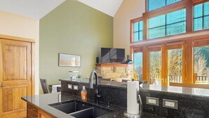 A kitchen with a granite countertop, a sink, a stone backsplash, and a window with blinds. - Centrally located with balcony, fireplace, heated garage parking & ski locker (Keystone)
