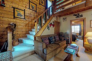 Un interior de madera con una escalera, un sofá con cojines estampados y una pequeña mesa con libros.