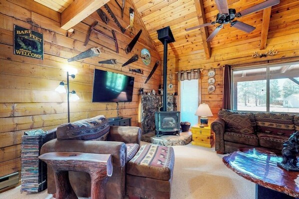 A rustic cabin interior with a fireplace, wooden walls, a television, and a cozy seating area.