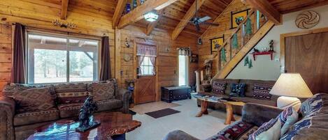 A log cabin interior with a large window, a staircase, and a fireplace.