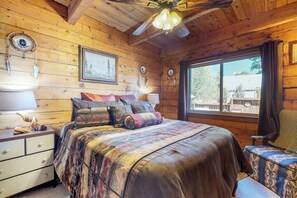 A wooden cabin bedroom with a bed, bedside lamps, a window, and a ceiling fan.