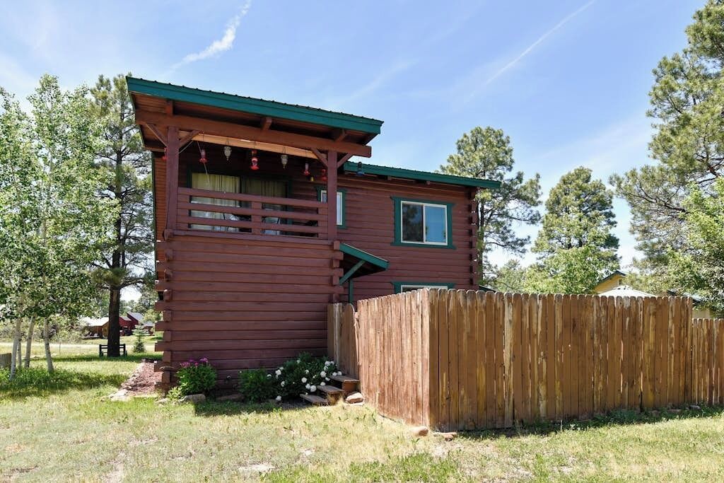 Une cabane en bois avec une véranda, une cour clôturée et une petite fenêtre.