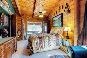 A wooden cabin bedroom with a bed, dresser, and a ceiling fan.
