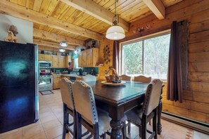 Interior de una cabaña de madera con una mesa de comedor, sillas, un refrigerador y una zona de cocina.