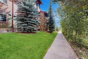 A residential building with a stone facade, a well-maintained lawn, and a concrete pathway. - Mountain resort condo with off-site pool, gym, ski gondola, game room & firepit (Steamboat Springs)