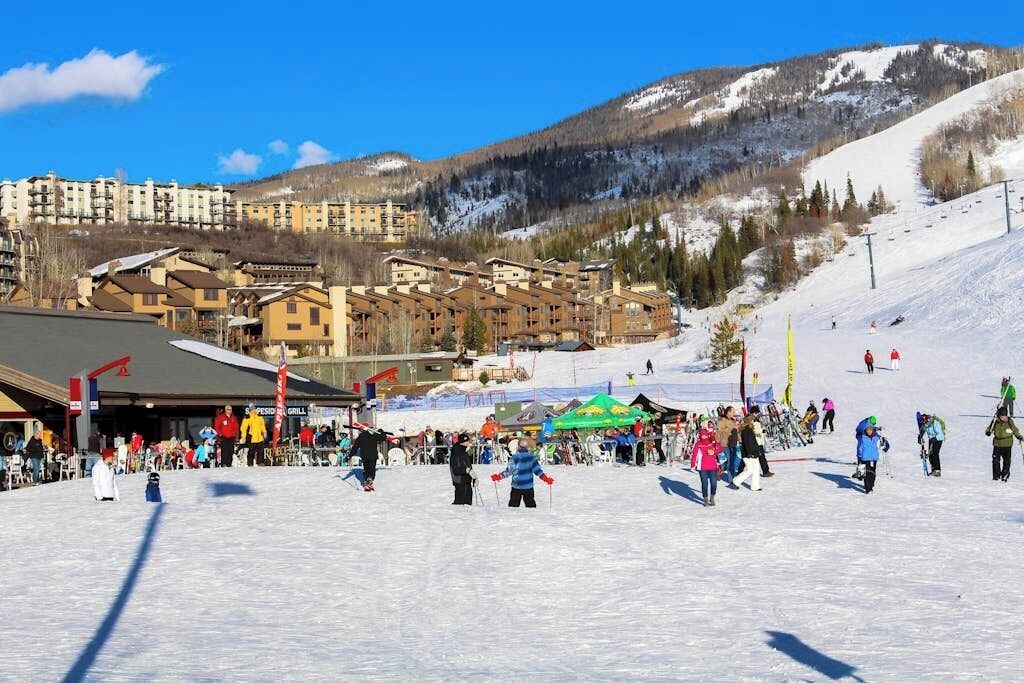 A ski resort with multiple buildings, a ski slope, and a crowd of people.