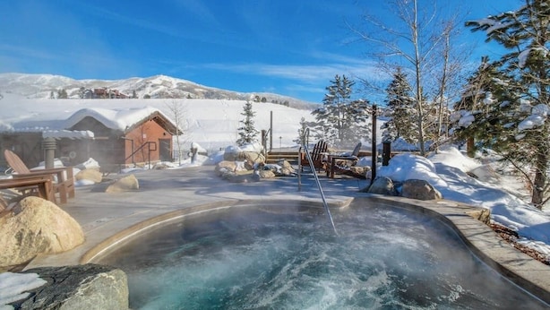 Ein Thermalbad mit einer Holzhütte, Liegestühlen und verschneiter Landschaft.