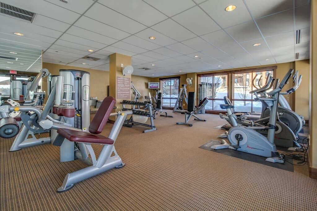 A gym with various exercise equipment, a television, and large windows.
