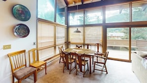 Een eetgedeelte met een houten tafel en stoelen, grote ramen en uitzicht op het omliggende landschap.