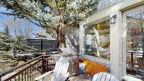 Terraza con una parrilla, sillas y vistas a árboles y una casa.