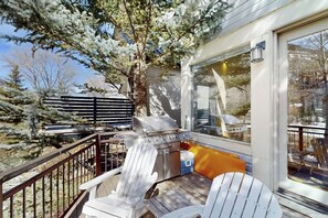 Eine Terrasse mit Grill, Stühlen und Blick auf Bäume und ein Haus.