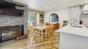 Een moderne keuken met een open haard, een houten eettafel en witte kasten.