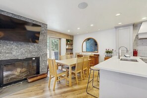 A modern kitchen with a fireplace, wooden dining table, and white cabinetry. - Charming condo w/ full kitchen, shared pool & hot tub - near ski resort (Vail)