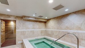 Uma área de spa com uma banheira de hidromassagem retangular, chuveiro e parede revestida de azulejos.