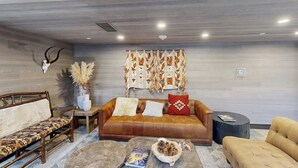 Uma sala de estar moderna com um sofá de couro, almofadas estampadas, uma mesa de centro com livros e uma tigela, e um enfeite na parede.
