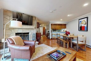 A living room with a fireplace, a sofa, a coffee table, and a TV mounted on the wall. - Conveniently located condo w/ fast wifi, shared hot tub & amazing location (Vail)