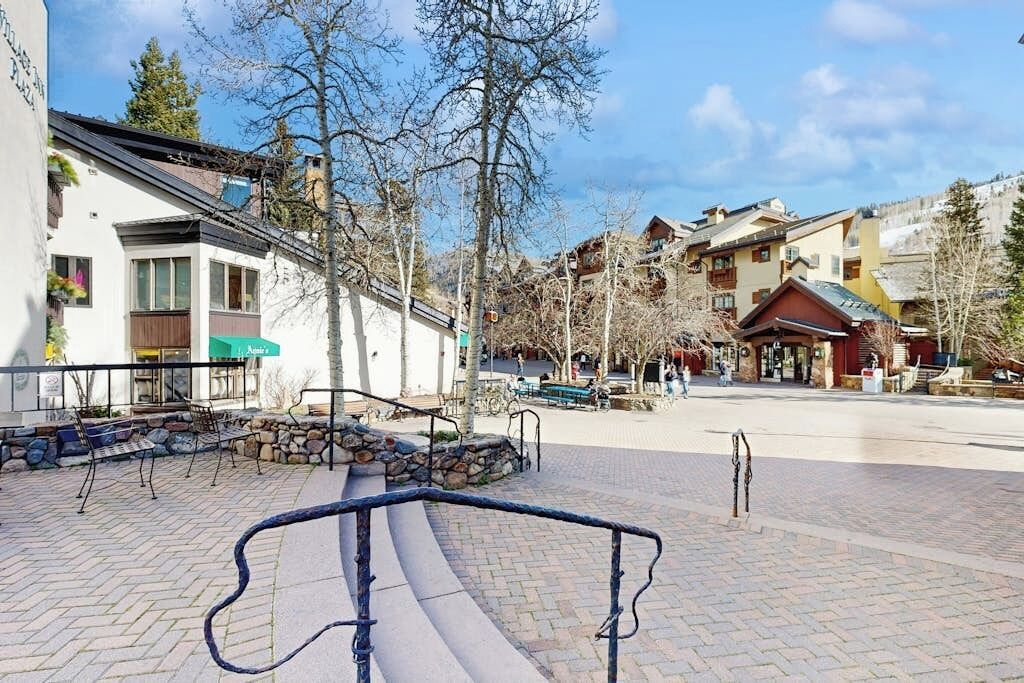Ein gepflasterter Platz mit Bänken, einer Steinmauer und Gebäuden mit Balkonen.