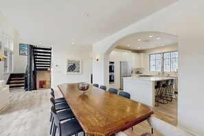 A modern kitchen with white cabinets, a wooden dining table, and a large island with bar stools. - Modern Vail retreat with golf course views, bus to slopes, and has a fireplace (Vail)