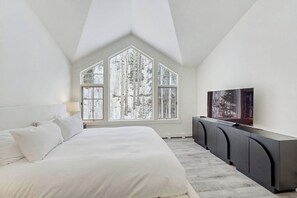 A bedroom with a large bed, a TV, and a window with a view of trees. - Modern Vail retreat with golf course views, bus to slopes, and has a fireplace (Vail)