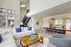 A spacious living area with a white sofa, a wooden coffee table, and a dining area with a long table and chairs. - Modern Vail retreat with golf course views, bus to slopes, and has a fireplace (Vail)
