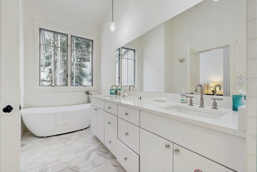 A modern bathroom with a freestanding bathtub, a large mirror, and a double sink vanity.