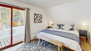 A bedroom with a bed, bench, nightstands, and a view through a sliding door. - Tranquil riverside cabin with mountain views and easy access to Breckenridge (Blue River)