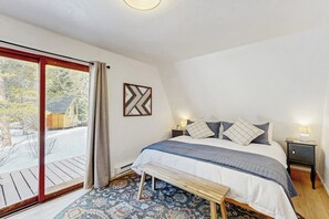 Ein Schlafzimmer mit Bett, Sitzbank, Nachttischen und Blick durch eine Schiebetür.