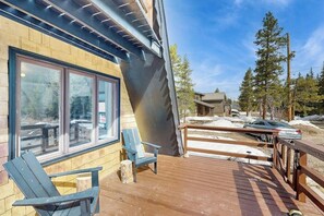Eine Holzterrasse mit zwei Stühlen, ein Gebäude mit großen Fenstern und eine verschneite Landschaft.
