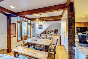 Un comedor con mesa y sillas de madera, una araña y una cocina con electrodomésticos modernos.