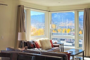 Ein Wohnzimmer mit einer Couch, einer Lampe und Blick auf Berge und Herbstlaub durch große Fenster.