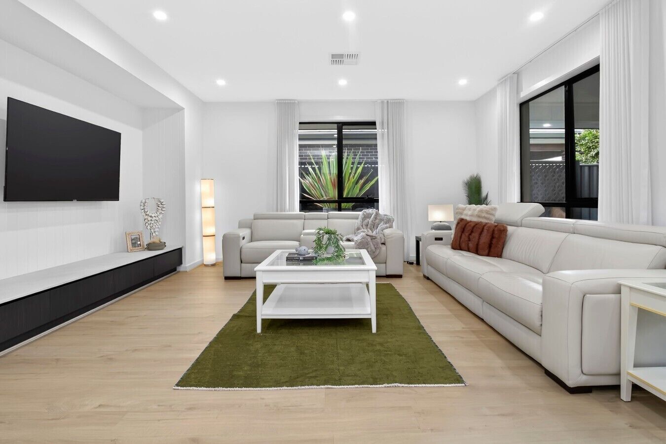 A modern living room with a flat-screen TV, two sofas, a coffee table, and a large window with curtains.