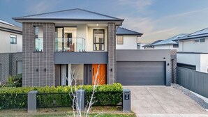 A modern two-story house with a garage, a balcony, and a well-maintained front yard.