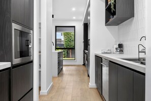 Een moderne keuken met donkere kastjes, een groot raam en uitzicht op een tuin.