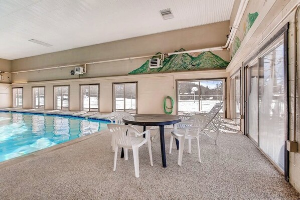 Une piscine intérieure avec des parois en verre transparent, une table avec des chaises et une fresque représentant une montagne sur le mur.
