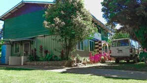 A house with a green roof, a white van parked in front, and a tree with pink flowers. - Shalom Mission Home (Mount Hagen)