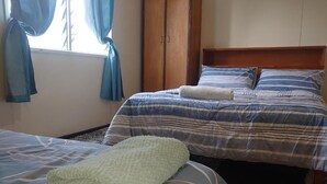 A bedroom with two beds, a wardrobe, and a window with curtains. - Shalom Mission Home (Mount Hagen)
