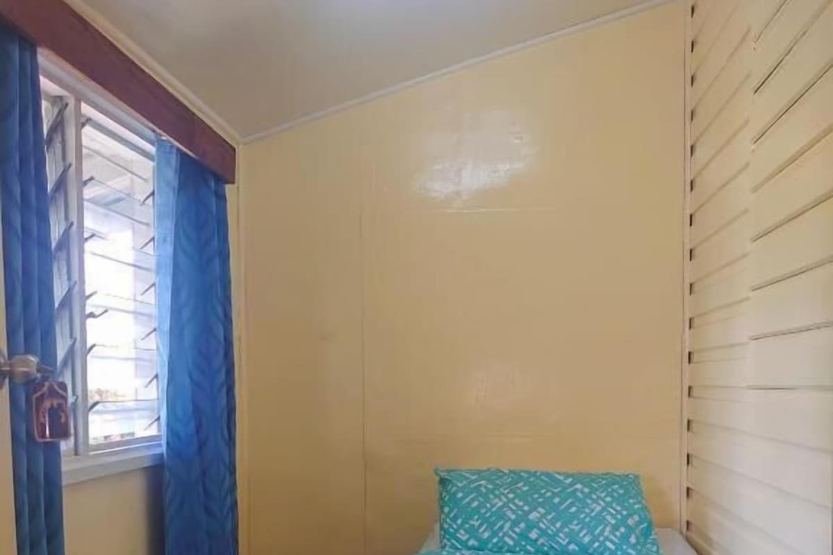Een kleine kamer met een enkel bed, een raam, een gordijn en een bed met een geborduurd beddegoed.
