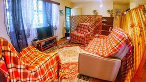 A living room with a sofa, armchairs, a TV, and a bookshelf. - Shalom Mission Home (Mount Hagen)