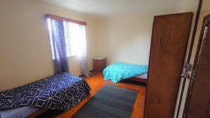 Un dormitorio con dos camas individuales, un armario de madera, una mesita de noche pequeña y una ventana con cortinas.