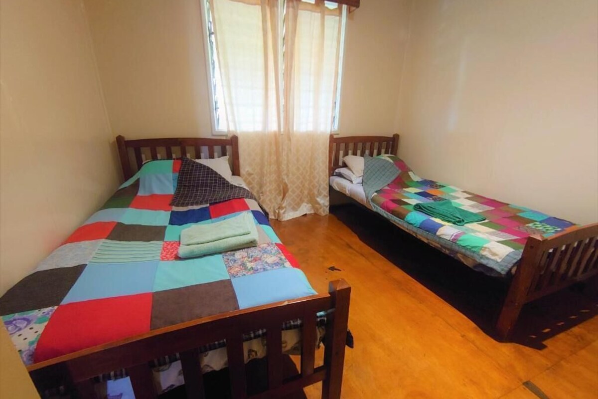 Een kamer met twee houten bedden, een raam met gordijnen en een houten vloer.